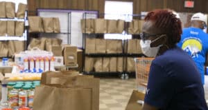 A woman in a mask looks out over brown paper bags filled with food for the community.