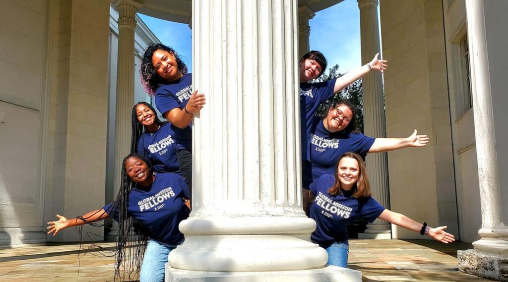 a group of smiling young people waving from behind a column