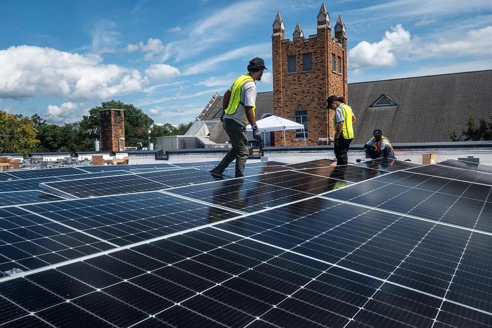 Workers install solar panels on church roof